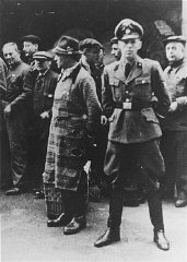 An SS officer stands in front of Jews assembled for...
