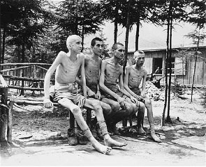 Four emaciated survivors sit outside in the newly liberated...