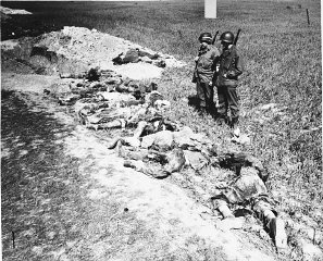 American soldiers look at the exhumed bodies of prisoners...