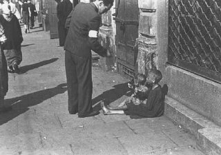 A Warsaw ghetto resident gives money to two children...